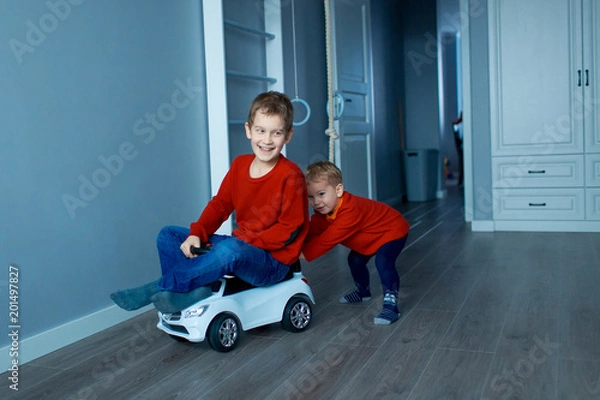 Obraz Two happy children riding on baby car in room, indoors.