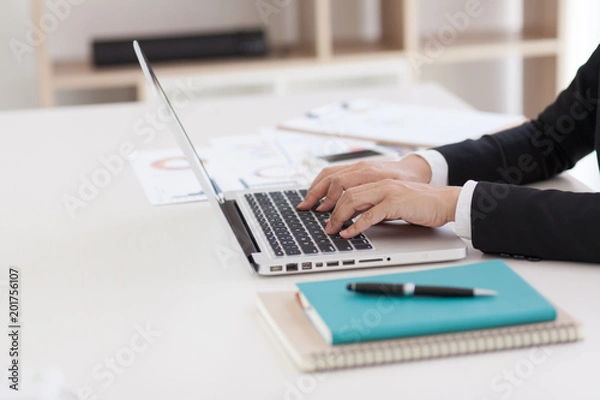 Fototapeta Businesswoman using laptop computer at working table - side view with document data graph.