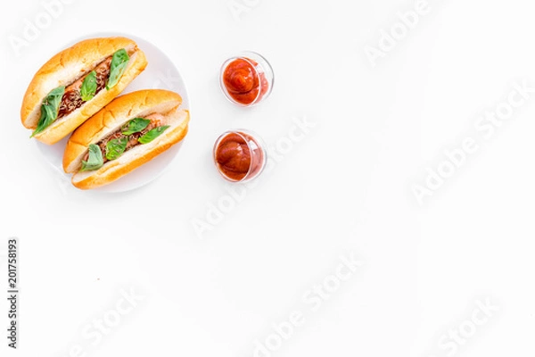 Fototapeta Fastfood concept. Make fresh hotdogs and home. bun for hot dogs with freid sausages and basil near tomato sause on white background top view space for text