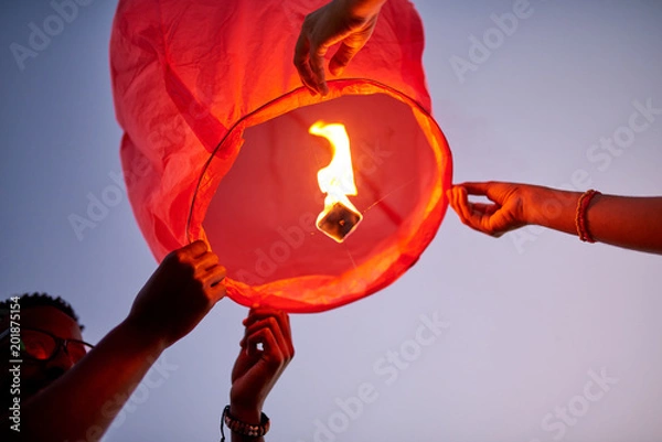 Fototapeta Below view of couple making wish and preparing to launch flying lantern to sky as symbol of eternal love outdoors
