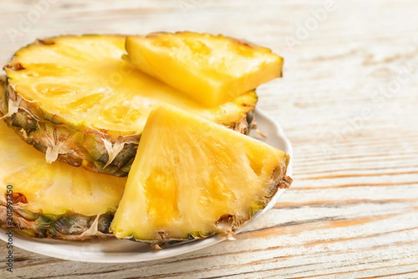 Fototapeta Plate with fresh pineapple slices on wooden background