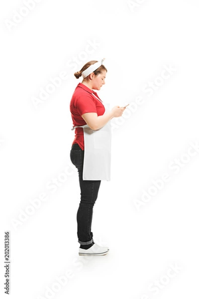 Fototapeta Portrait of cute smiling woman with mobile phone in her hands in the studio, isolated on white background