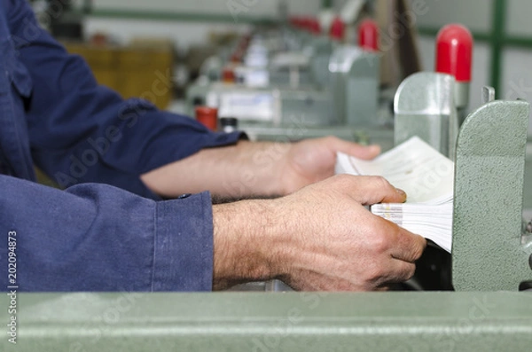 Fototapeta Man working on print production stitching machine in printing factory. Industrial workers