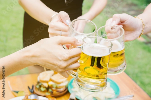 Fototapeta Close-up cropped image of friends clinking with beer in garden.