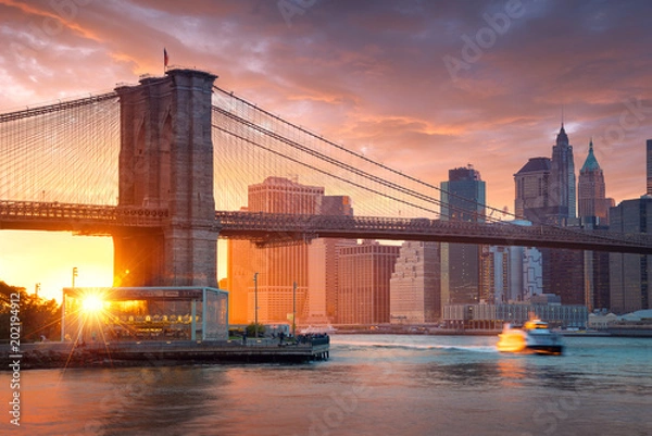 Obraz Słynny Brooklyn Bridge w Nowym Jorku z dzielnicą finansową - centrum Manhattanu w tle. Statek wycieczkowy po East River i piękny zachód słońca nad Jane's Carousel.