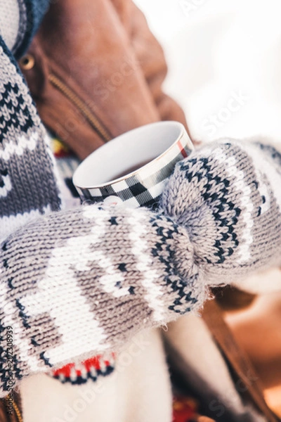 Obraz a girl in warm mittens with patterns holds a cup of hot tea in the street in the winter