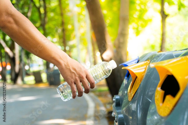 Fototapeta Closeup man hand throwing empty plastic water bottle into to recycling bin, environmental protection concept.