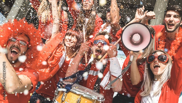Fototapeta Przyjaciele kibiców piłki nożnej kibice z konfetti oglądający mecz piłki nożnej na stadionie - grupa młodych ludzi z czerwonymi koszulkami, podekscytowana zabawą na mistrzostwach świata
