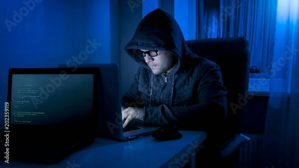 Fototapeta Portrait of hacker criminal working on laptop at night