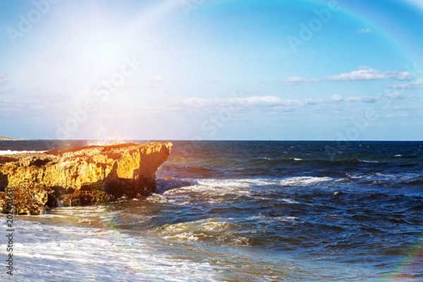 Fototapeta Waves crashing against rocks on the shore of the Caribbean Sea in Cozumel Mexico with colorful rainbow sun flare
