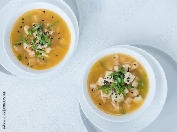 Fototapeta Ceramic bowl of traditional asian soup with spring onion, chicken, tofu and sesame. Top view. Concept minimal food.