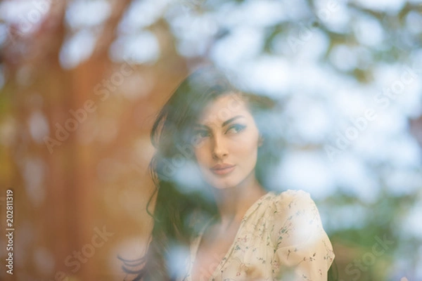 Obraz beautiful mysterious caucasian girl in summer dress behind window with reflections of trees