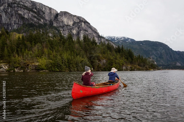 Fototapeta Adventurous people on a wooden canoe are paddling in a river with beautiful rocky mountain in the background. Taken in Squamish, North of Vancouver, BC, Canada.
