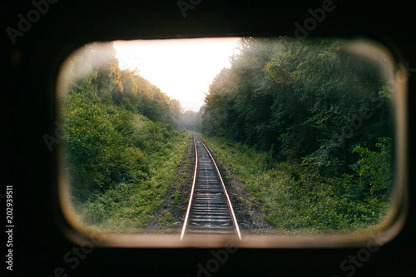 Obraz Train travel. Beautiful far scenic view through window from riding train at railway with nature ladnscape at sunset. Tourist trip. Atmospheric lifestyle journey.  End of weekend.  Farewell vacation.