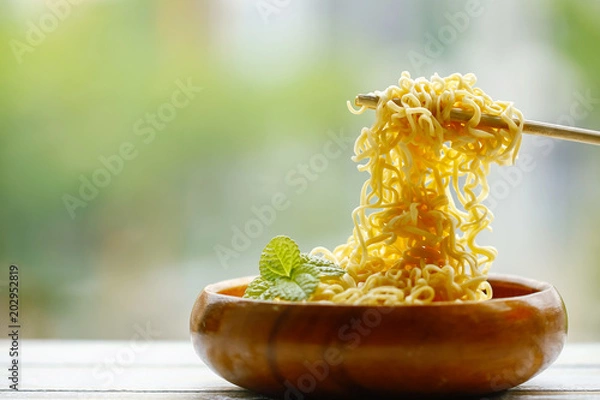 Obraz Instant noodle in wooden bowl with bamboo chopstick on green background