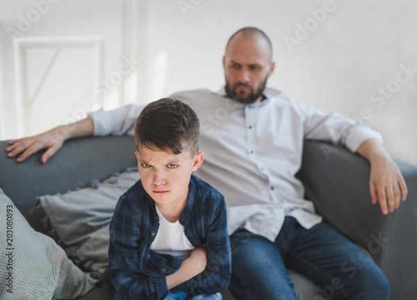 Fototapeta A sad and resentful boy and an angry father in the background.