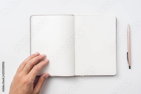 Fototapeta Design concept - Top view of man's hand holding hardcover gray linen notebook  and ballpoint pen isolated on white background for mockup