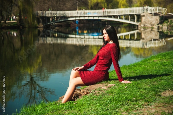 Obraz  beautiful young brunette with long hair in a park on a spring in spring among flowering trees in a red dress in hands holds magnolia flowers