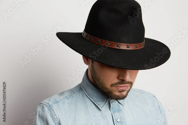 Fototapeta Portrait of a pensive caucasian man in hat wearing denim shirt and looking down isolated on white background