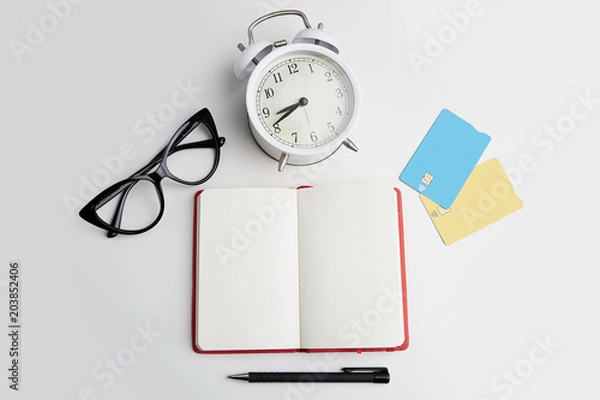 Fototapeta Mockup of two blank credit cards, headphones, eye glasses and retro alarm clock on empty white desk. Business empty mock-up background for message writing.Top view concept