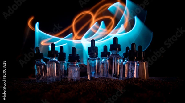 Fototapeta Vape concept. Smoke clouds and vape liquid bottles on dark background. Light effects. Useful as background or vape advertisement or vape background.