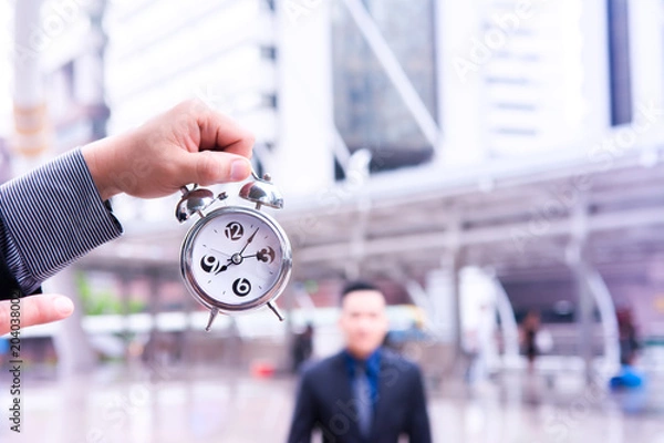 Fototapeta Blured business man is standing behind the clock that hold by another for motivate him.