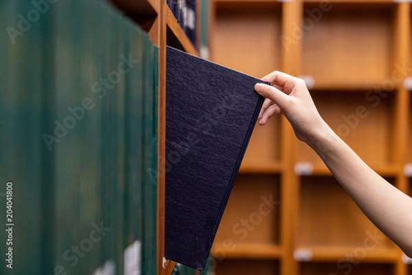 Fototapeta Hand pulling a Thesis book off the shelf in Library. Green colors books.