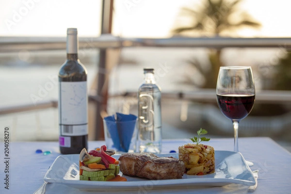 Fototapeta table in a restaurant on the background of the ocean. meat with garnish in a restaurant