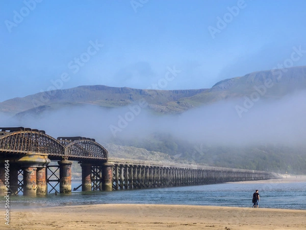 Fototapeta Sea mist rolls in at the Barmouth pedestrian and railway bridge, the longest viaduct in Wales, UK. Situated over the River Mawddach at Barmouth. Used by cyclists too.