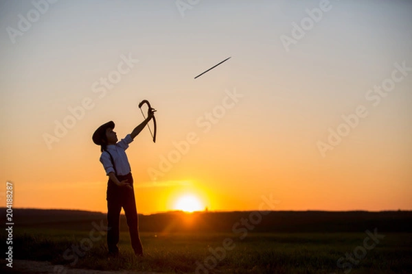 Fototapeta Silhouette of child playing with bow and arrows, archery shoots a bow at the target.