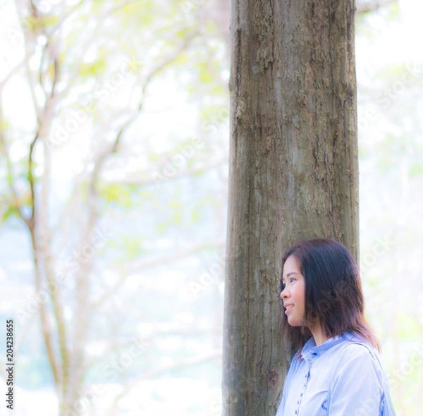 Fototapeta Woman is standing close to the tree feel relax by her eys that look forward in the garden with blur and soft background