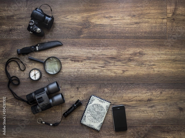 Fototapeta on a dark wooden background passport map camera magnifier lantern compass binoculars phone smartphone knife hiking trip vacation
