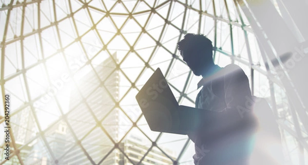 Fototapeta Silhouette of young intelligent man managing a computer in modern office environment with copy space for your text message or promotional content.