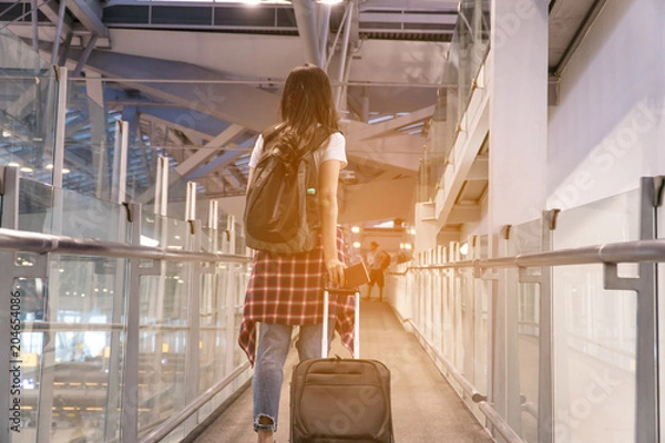 Fototapeta Young woman pulling suitcase in modern airport terminal. Travelling guy with his luggage while waiting for transport. Rear view. holiday vacation concept. Copy space.