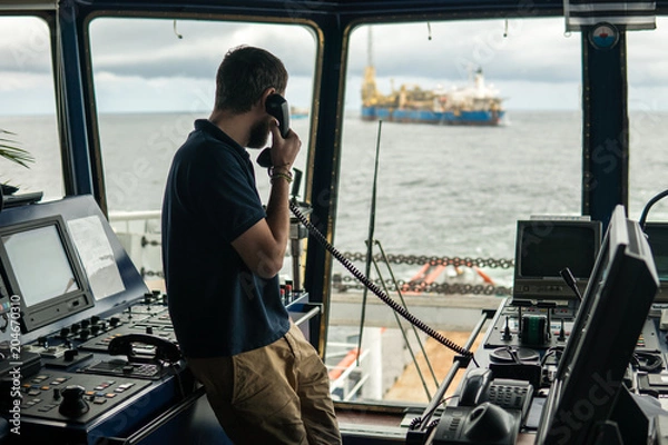 Fototapeta Deck navigation officer on the navigation bridge. He speaks by VHF radio, GMDSS Watchkeeping, collision prevention at sea. COLREG
