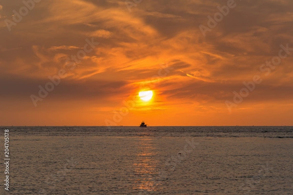 Obraz A ship at sea in the sunset with orange sky
