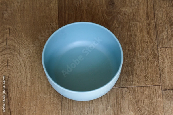 Obraz Empty blue plastic bowl on wooden background, above view