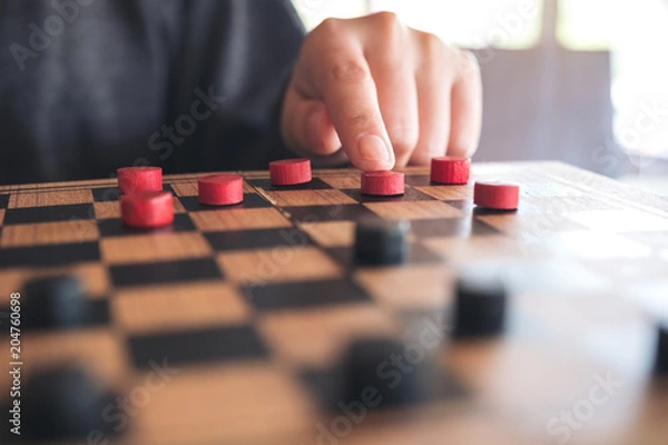 Fototapeta Closeup image of people playing and moving checkers in a chessboard
