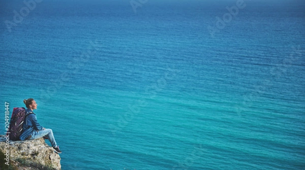 Fototapeta Profile of glad woman with rucksack relaxing on hill and observing blue water of calm ocean. Copy space in right side