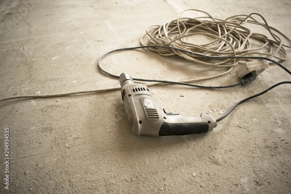 Fototapeta the old electric drill rests on the concrete floor, near the extension cord with a socket