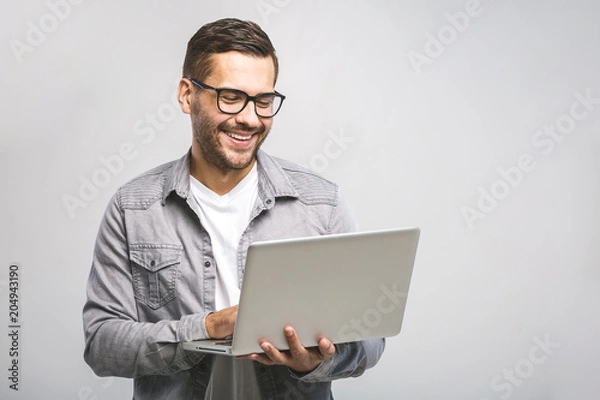 Fototapeta Confident business expert. Confident young handsome man in shirt holding laptop and smiling while standing against white background