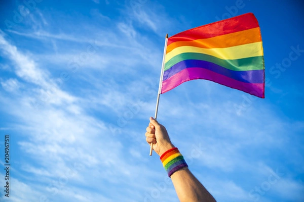 Fototapeta Colorful backlit rainbow gay pride flag being waved in the breeze against a sunset sky.