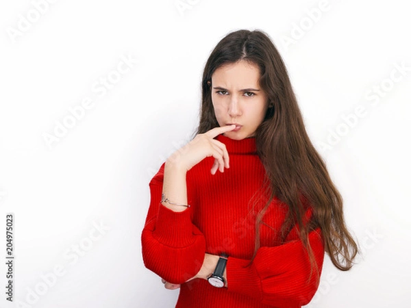 Obraz Young beautiful brunette woman in red sweater showing suspicious emotion posing against white background