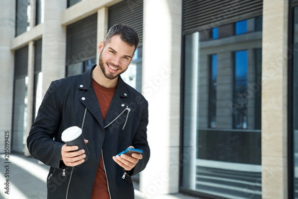 Fototapeta Portrait of handsome man with beard with cheerful positive emotions walking down the street on Sunny day with Cup of coffee