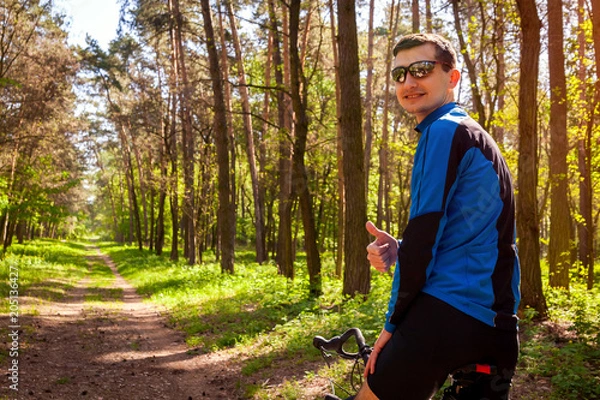Fototapeta Happy young man bicyclist riding a road bike in spring forest. Man showing hand with thumb up.
