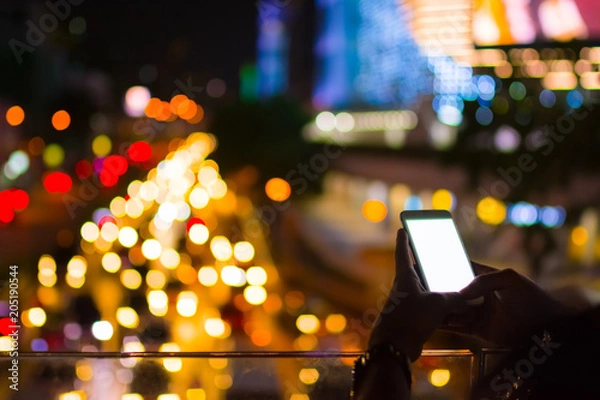 Fototapeta Two hands of man playing smartphone with bright white monitor on colorful bokeh background for hi technology concept that look like advance