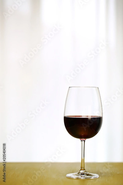 Fototapeta Single Red Wine in Bordeaux-shaped glass on Right Side of Copper Counter Top, with defocused Window and White Curtain, plain background, No decoration, Ambient Nature Day Lighting Studio image 1