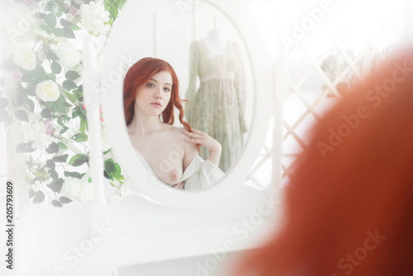 Fototapeta Tender portrait of a young dreamy redhead woman wearing beautiful vintage dress. She is sitting in front of the mirror with naked breast.