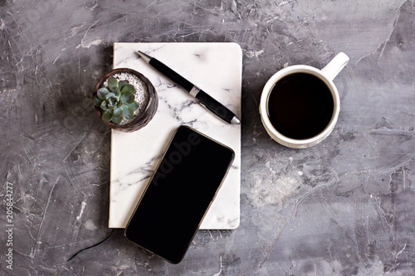 Obraz Notepad, mobile phone, pen, succulent, glasses, cup of coffee on a gray cement background.