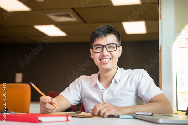 Fototapeta Young handsome cute Asian men student smiles and do homeworks in university